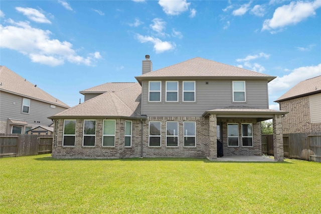rear view of house featuring a patio, a chimney, a lawn, brick siding, and a fenced backyard
