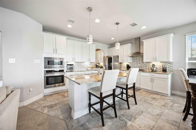 kitchen with wall chimney exhaust hood, visible vents, appliances with stainless steel finishes, and tasteful backsplash