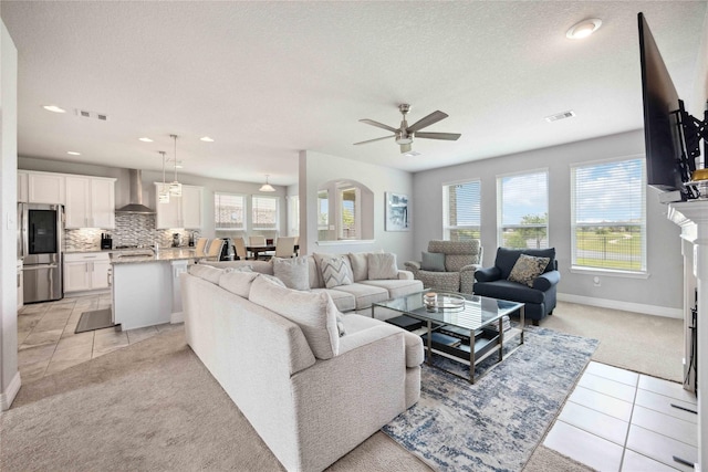 living room featuring light colored carpet, baseboards, visible vents, a ceiling fan, and light tile patterned flooring