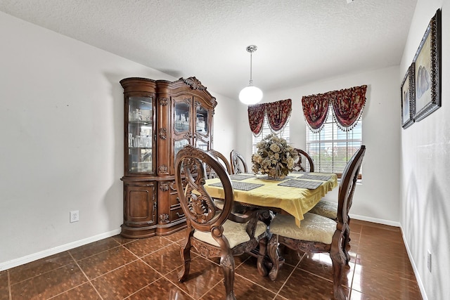 dining space with baseboards, a textured ceiling, and dark tile patterned flooring