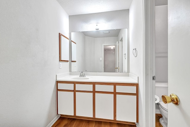 bathroom featuring a textured wall, baseboards, toilet, wood finished floors, and vanity
