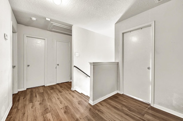 corridor with attic access, a textured ceiling, an upstairs landing, and wood finished floors