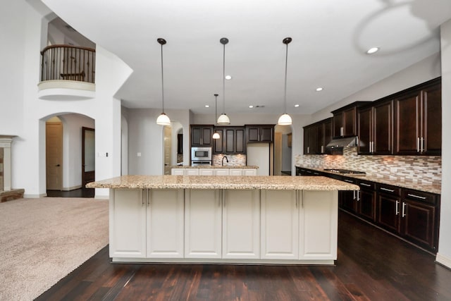 kitchen with dark brown cabinets, appliances with stainless steel finishes, arched walkways, tasteful backsplash, and under cabinet range hood