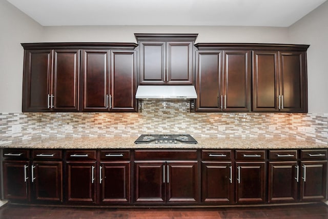 kitchen with dark brown cabinets, light stone counters, stainless steel gas stovetop, tasteful backsplash, and under cabinet range hood