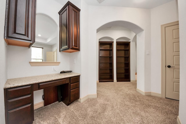 unfurnished office featuring baseboards, light carpet, and built in study area