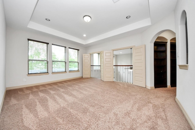 unfurnished bedroom featuring baseboards, carpet, a tray ceiling, and arched walkways