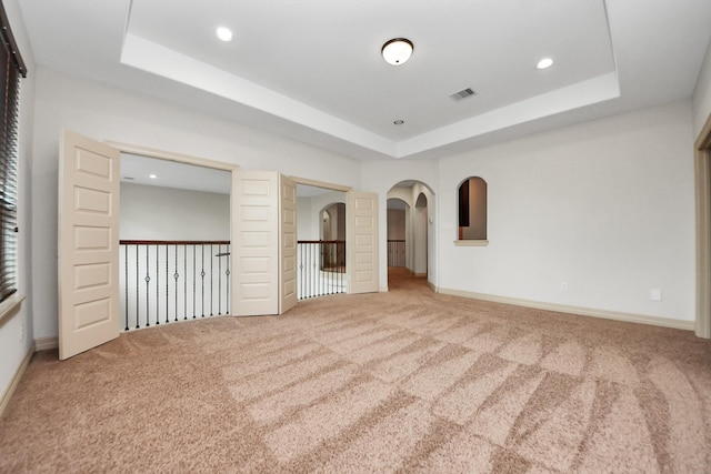 unfurnished bedroom featuring carpet floors, arched walkways, visible vents, and a raised ceiling