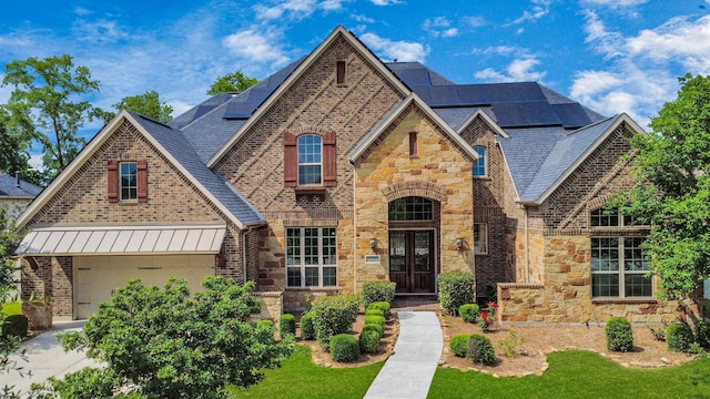 view of front of house with a standing seam roof, french doors, a garage, roof mounted solar panels, and stone siding