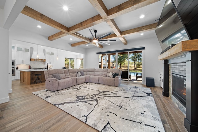 living room with beam ceiling, a ceiling fan, a fireplace, and light wood-style flooring