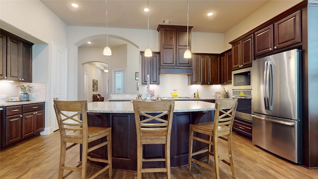 kitchen with light wood finished floors, arched walkways, stainless steel appliances, backsplash, and a kitchen island