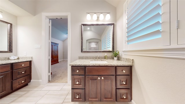 bathroom with tile patterned flooring, lofted ceiling, baseboards, two vanities, and a sink