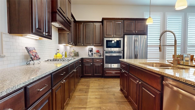 kitchen with decorative light fixtures, appliances with stainless steel finishes, a sink, light stone counters, and light wood finished floors