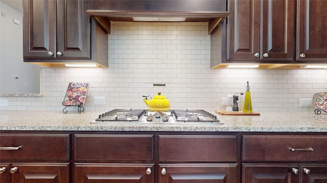 kitchen with light stone countertops, backsplash, dark brown cabinets, and stainless steel gas stovetop