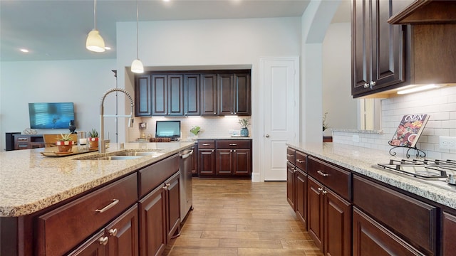 kitchen with decorative light fixtures, tasteful backsplash, light stone countertops, wood finished floors, and a sink
