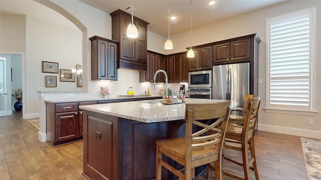 kitchen with decorative backsplash, dark brown cabinets, baseboards, stainless steel appliances, and light wood-style flooring