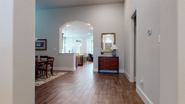 hallway with arched walkways, baseboards, and dark wood finished floors