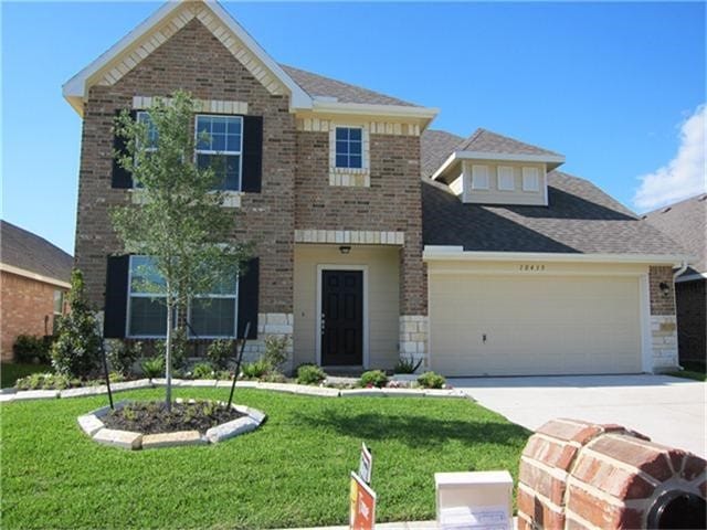 traditional home with a front lawn, concrete driveway, brick siding, and a garage