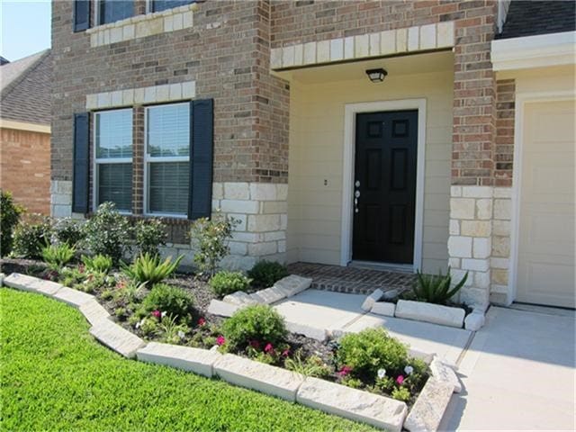 property entrance featuring driveway, a shingled roof, brick siding, and stone siding