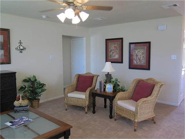 living area with baseboards, visible vents, a ceiling fan, and carpet