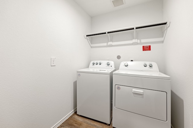 washroom with laundry area, visible vents, baseboards, washer and dryer, and wood finished floors