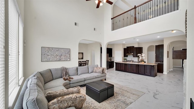 living room featuring baseboards, arched walkways, a ceiling fan, marble finish floor, and a high ceiling
