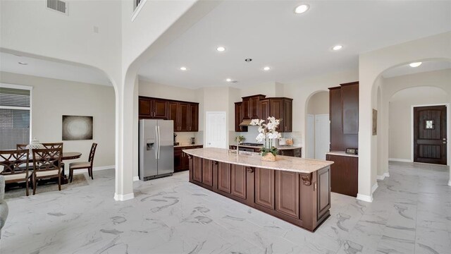 kitchen featuring arched walkways, stainless steel fridge, marble finish floor, baseboards, and visible vents