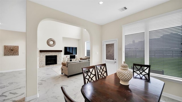 dining space with a fireplace, marble finish floor, visible vents, baseboards, and arched walkways