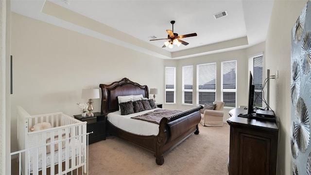bedroom with visible vents, a raised ceiling, a ceiling fan, and light colored carpet