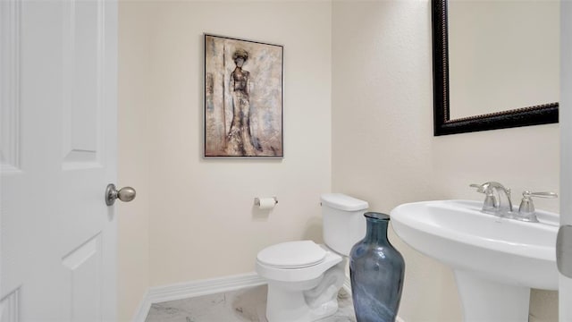 bathroom with toilet, baseboards, marble finish floor, and a sink