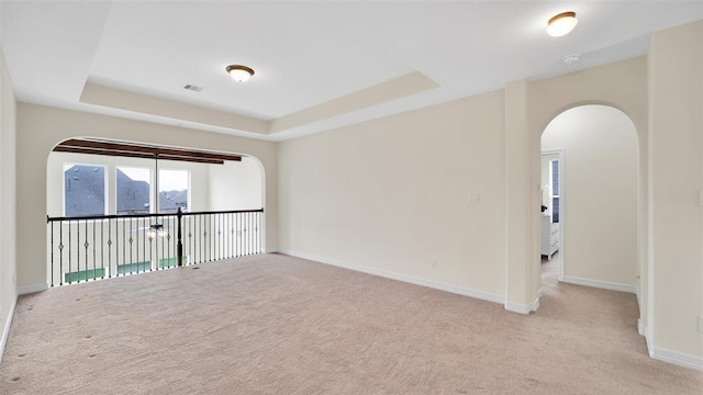unfurnished room with a tray ceiling, visible vents, carpet, baseboards, and arched walkways