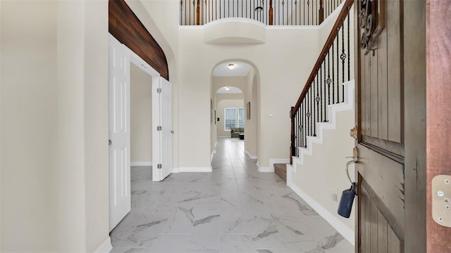 entrance foyer with arched walkways, stairway, marble finish floor, and baseboards