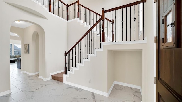 staircase with a towering ceiling, arched walkways, marble finish floor, and baseboards
