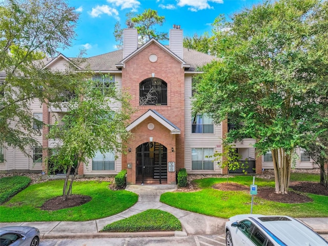 8051 Bay Branch Dr Unit 424, The Woodlands, TX 77382 - view of front of house featuring roof with shingles, a chimney, a front lawn, and brick siding