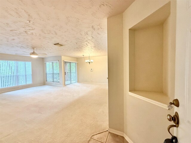 spare room with light colored carpet, a textured ceiling, ceiling fan with notable chandelier, baseboards, and visible vents