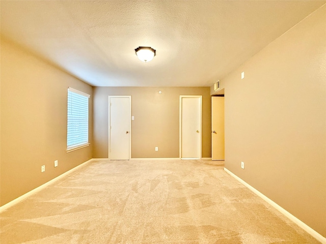 spare room with a textured ceiling, baseboards, light colored carpet, and visible vents