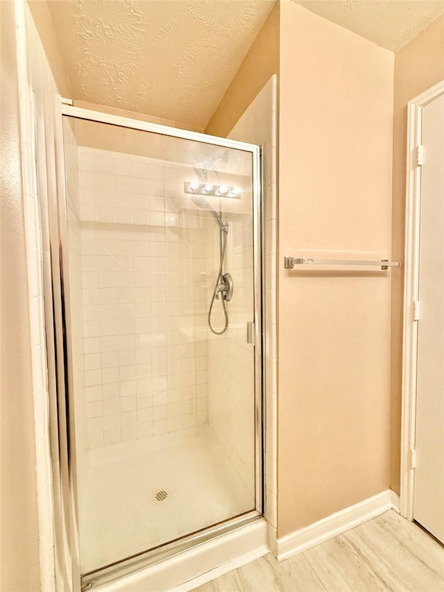 bathroom featuring a textured ceiling, baseboards, and a stall shower