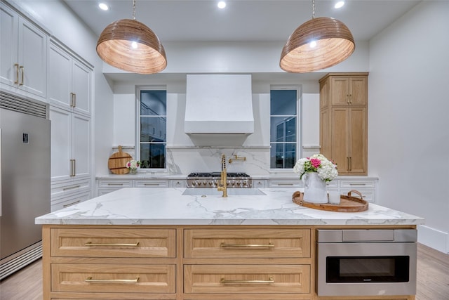 kitchen featuring light wood finished floors, tasteful backsplash, light stone counters, wall chimney range hood, and stainless steel built in refrigerator