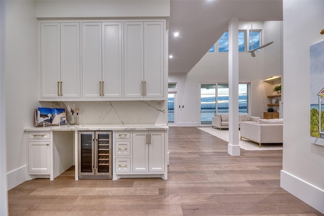 bar featuring tasteful backsplash, beverage cooler, light wood-style flooring, a high ceiling, and a dry bar