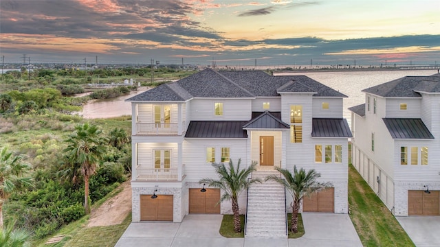 view of front of home with a standing seam roof, a garage, a balcony, metal roof, and driveway