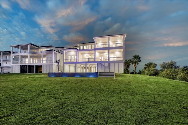 back of property at dusk featuring a yard and a balcony