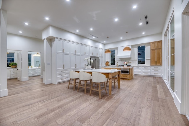 kitchen with a breakfast bar, light countertops, a large island, light wood-type flooring, and premium range hood