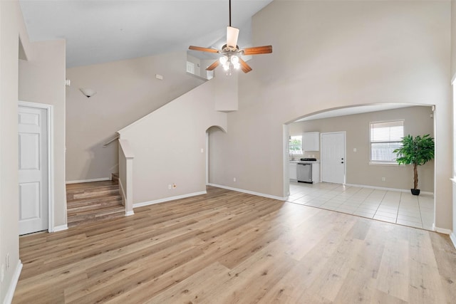 unfurnished living room featuring light wood-style flooring, stairway, arched walkways, a ceiling fan, and high vaulted ceiling
