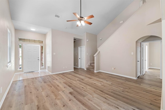 unfurnished living room with visible vents, arched walkways, ceiling fan, baseboards, and light wood-type flooring