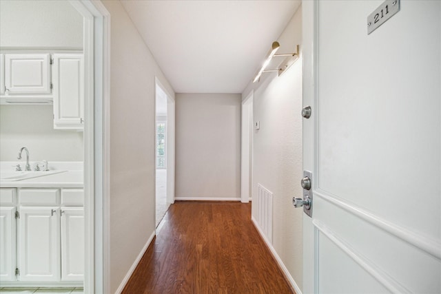 hallway with dark wood-style floors, visible vents, baseboards, and a sink