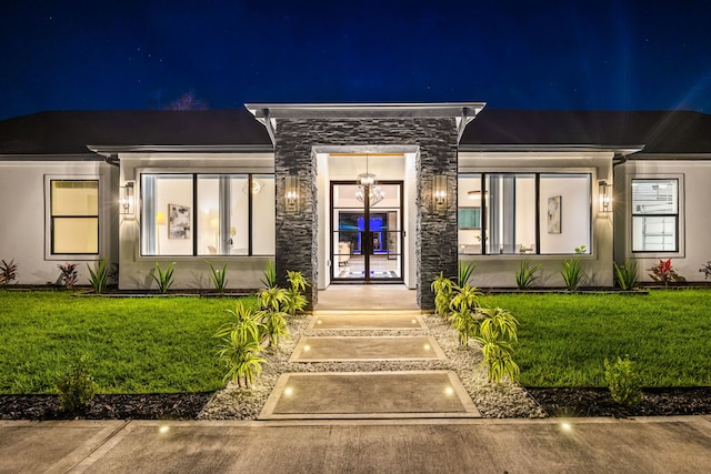 exterior entry at night with a yard, stone siding, and stucco siding