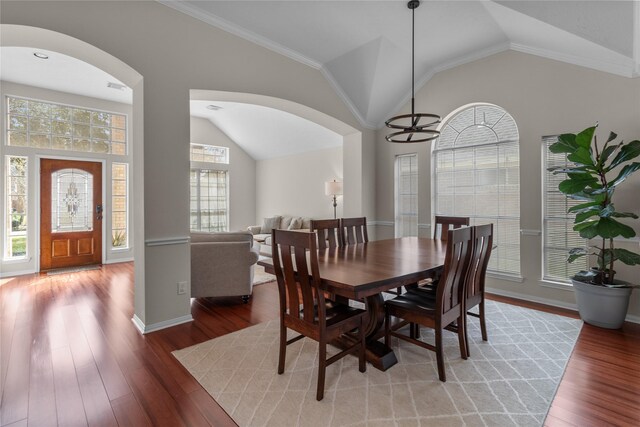dining room featuring arched walkways, lofted ceiling, wood finished floors, and baseboards