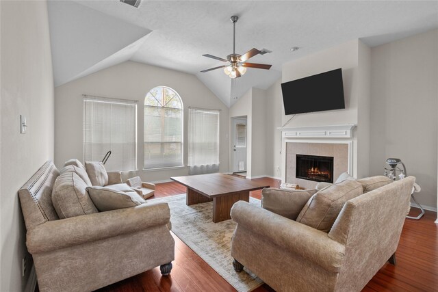 living room with a tile fireplace, vaulted ceiling, wood finished floors, a ceiling fan, and baseboards