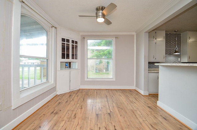 unfurnished dining area featuring a wealth of natural light, ornamental molding, a ceiling fan, and light wood finished floors