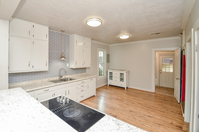 kitchen with light wood finished floors, a sink, black electric cooktop, visible vents, and light countertops
