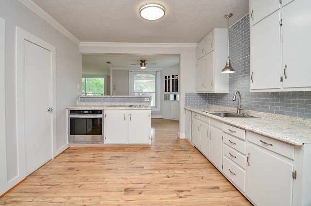 kitchen with white cabinetry, light wood finished floors, stainless steel oven, and a sink
